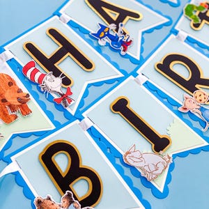 May include: A blue banner with the word "HAPPY" spelled out in black and gold letters. Each letter is on a light blue pennant with a scalloped edge. The pennants are decorated with cartoon characters.