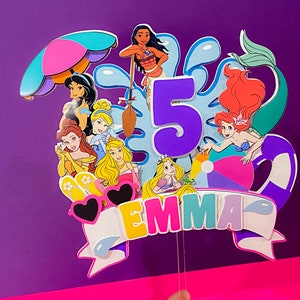 May include: A colorful cake topper featuring Disney princesses, a beach umbrella, a beach ball, and the number 5. The topper also includes the name "Emma".
