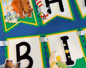 Può includere: Uno striscione decorativo con gagliardetti bianchi dai bordi verdi smerlati, lettere nere e illustrazioni di personaggi delle fiabe, tra cui un orso bruno, un gatto col cappello e una piccola figura seduta su una luna crescente.