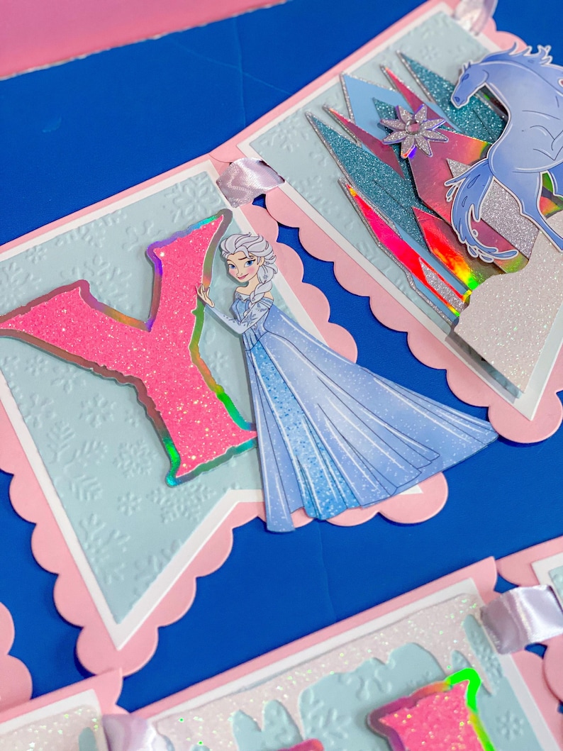 Może przedstawiać: Baner o tematyce księżniczki, z jasnoniebieskim tłem i r&oacute;żowymi, falistymi krawędziami. Baner zawiera r&oacute;żową literę "Y" z brokatem i ilustrację księżniczki w niebieskiej sukni. Dodatkowe elementy to niebieski koń i zamek.