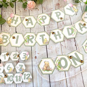 May include: A Winnie the Pooh themed birthday banner with green and yellow hexagonal pieces that spell out "Happy Birthday One". The banner is decorated with bees, flowers, and Winnie the Pooh characters. There are also 12 smaller hexagonal pieces with numbers 1 through 12 and Winnie the Pooh characters.