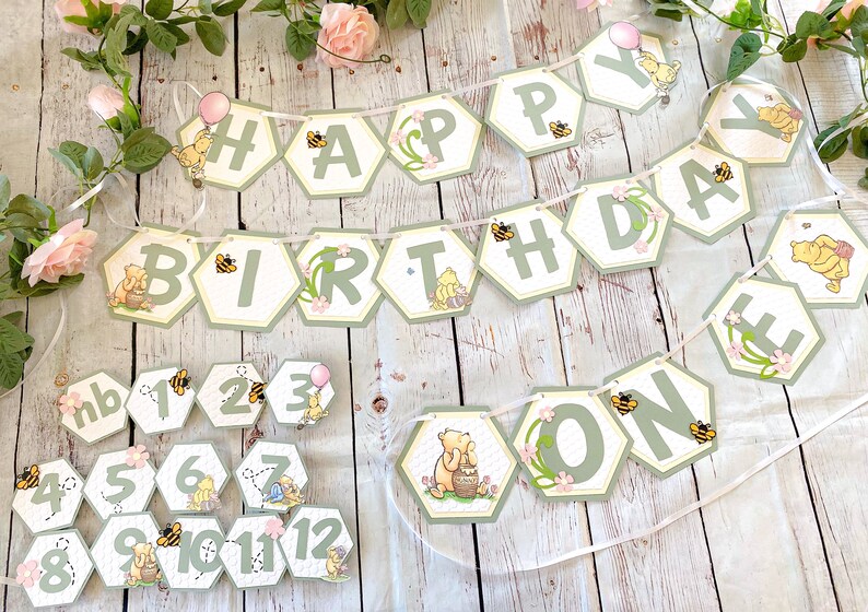 May include: A Winnie the Pooh themed birthday banner with green and yellow hexagonal pieces that spell out "Happy Birthday One". The banner is decorated with bees, flowers, and Winnie the Pooh characters. There are also 12 smaller hexagonal pieces with numbers 1 through 12 and Winnie the Pooh characters.