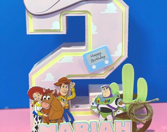 Può includere: Una decorazione tridimensionale a forma di numero due con sfondo rosa chiaro a motivi nuvolosi, sormontata da un cappello da cowboy bianco e una stella gialla. Include sagome di Jessie, Bullseye, Woody e Buzz Lightyear, un cactus verde, una ruota di carro marrone e il nome MARIAH in stampatello.