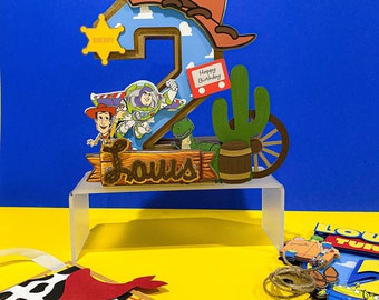May include: A colorful, layered cake topper featuring the number 2 with a cowboy hat, sheriff badge, and characters from a popular animated film. Includes a sign that says "Happy Birthday" and a wooden sign that says "Louis".