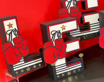 May include: Black and white letters "LEG" with red boxing gloves and gold stars. The letters are decorated with a black and white boxing ring design.