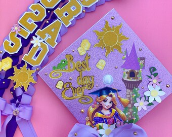 Puede incluir: Un gorro de graduación morado y dorado decorado con una princesa, un sol y las palabras "Best day Ever". El gorro está adornado con un lazo morado y purpurina dorada. También se muestra un collar de graduación morado y dorado con las palabras "Congrats" y "Grad".