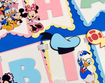 Può includere: Uno striscione decorativo in carta con personaggi Disney tra cui Topolino, Minnie, Paperino, Paperina e Pluto. Lo striscione è composto da gagliardetti con bordi smerlati in colori pastello, grandi lettere, decorazioni floreali bianche e clip argentate.