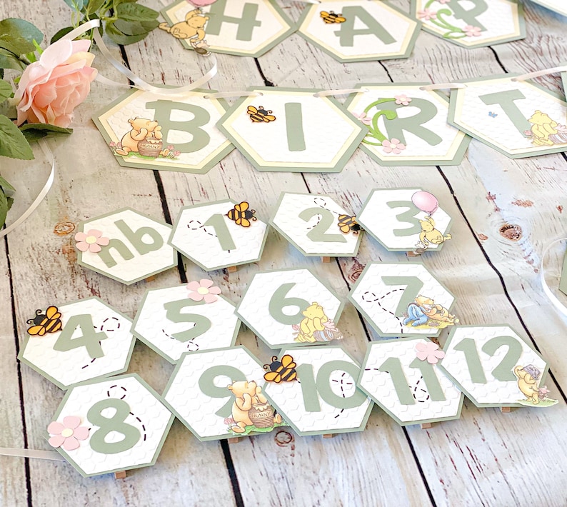 May include: Winnie the Pooh themed birthday party decorations with green and yellow honeycomb shaped paper cutouts. The cutouts feature Winnie the Pooh characters, bees, and the words "Happy Birthday".
