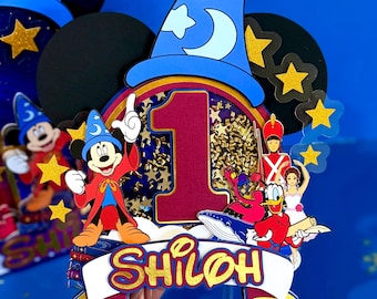 Può includere: Un topper per torta in carta a strati con un grande numero uno rosso, un cappello da mago blu e personaggi dei cartoni animati tra cui un topo in tunica, un papero e un soldato. Include coriandoli a forma di stella dorata e il nome SHILOH.