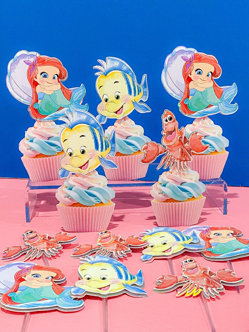 May include: A set of cupcake toppers featuring characters from The Little Mermaid. The toppers include Ariel, Flounder, and Sebastian. The toppers are printed on cardstock and are perfect for adding a touch of Disney magic to your cupcakes.
