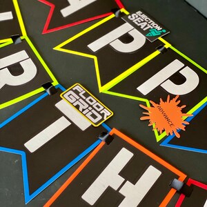 May include: A black and white banner with the word "HAPPY" spelled out in white letters. Each letter is on a separate black flag with a colorful border. The flags are connected with black ribbon. There are small colorful stickers on each flag.