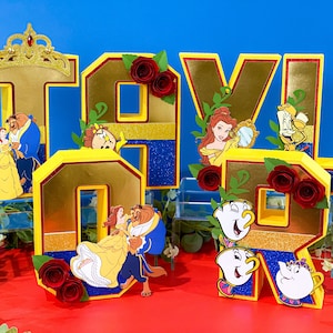 May include: Gold glitter letters spelling "TAVIOR" with various Disney characters from Beauty and the Beast, including Belle, Beast, and Cogsworth. The letters are decorated with red roses and green leaves.