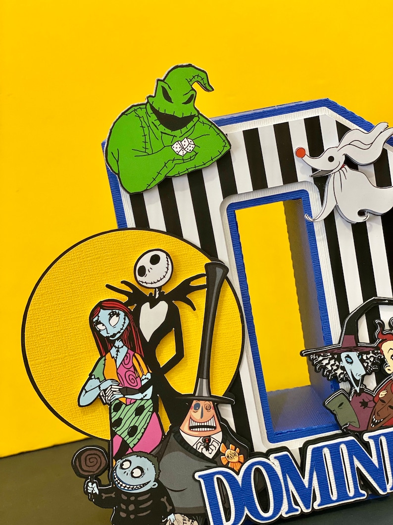 Puede incluir: Una creaci&oacute;n de papel 3D con los personajes de la pel&iacute;cula Pesadilla antes de Navidad. Los personajes incluyen a Jack Skellington, Sally, Oogie Boogie y Zero. La creaci&oacute;n est&aacute; decorada con rayas blancas y negras y la palabra "DOMIN" est&aacute; escrita en letras azules.