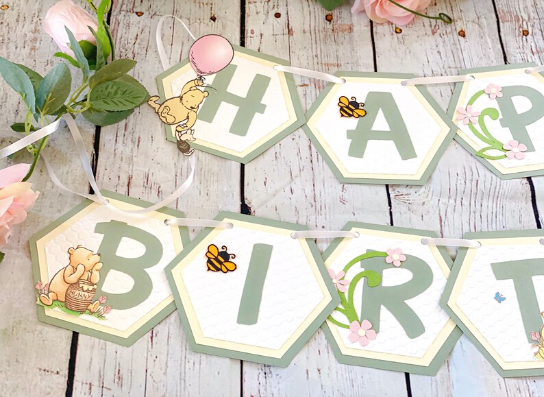May include: A green and yellow Winnie the Pooh themed banner with the words "Happy Birthday" in green letters. The banner is decorated with bees, flowers, and Winnie the Pooh characters.