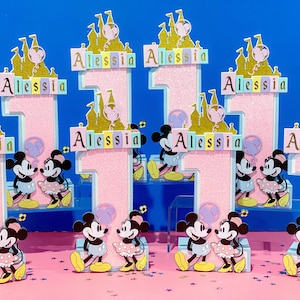 May include: Set of pink and white number one cake toppers with a castle and Mickey Mouse and Minnie Mouse characters. The toppers say "Alessia" on each one.