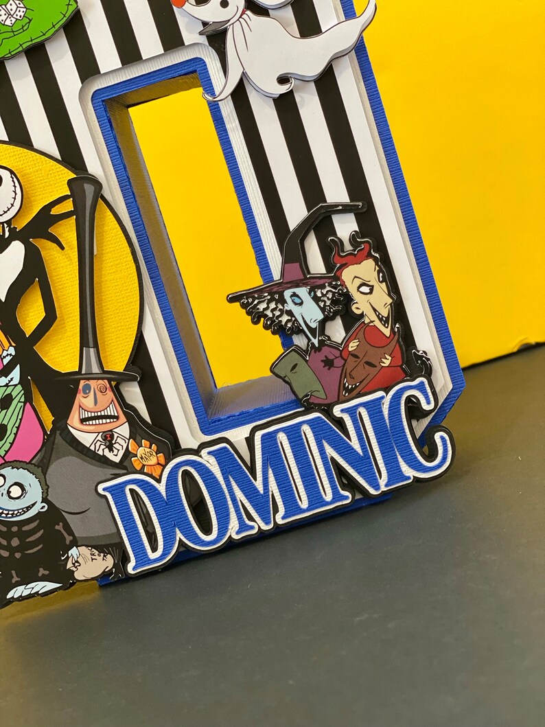 Puede incluir: Un fondo a rayas blanco y negro con un borde azul. El nombre "DOMNIC" est&aacute; escrito en letras blancas con un contorno azul. Hay varios personajes de la pel&iacute;cula "Pesadilla antes de Navidad" en el fondo.