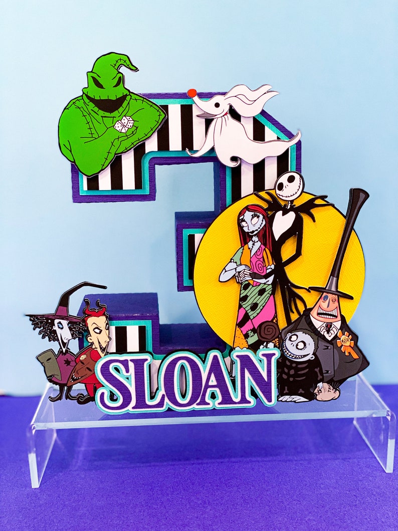 K&ouml;nnte beinhalten: Ein 3D-Tortenaufsatz mit Figuren aus Nightmare Before Christmas. Der Aufsatz ist in Form der Zahl 3 gestaltet und enth&auml;lt Figuren wie Jack Skellington, Sally, Oogie Boogie und Zero. Der Aufsatz ist mit schwarzen und wei&szlig;en Streifen und einem gelben Mond verziert. Der Name "SLOAN" ist in lila und t&uuml;rkisfarbenen Buchstaben geschrieben.