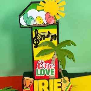 May include: A colourful papercraft number one with a reggae theme. It features a yellow sun, green palm tree, red, yellow, and green birds, a musical note, a drum, a guitar, and the words "One Love" and "IRIE".