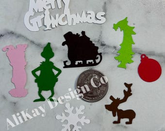 May include: A set of paper cutouts featuring a Grinch theme. The set includes a white snowflake, a green Grinch, a red ornament, a brown reindeer, a green Christmas tree, a black sleigh, and a white sign that reads "Merry Grinchmas".
