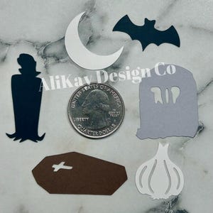 May include: A set of Halloween-themed paper cutouts, including a black vampire, a white crescent moon, a black bat, a white garlic, a brown coffin with a white cross, and a gray tombstone with the word "RIP" cut out.