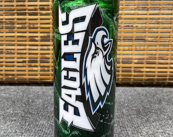 Puede incluir: Un vaso marmoleado verde y blanco con un logotipo de los Philadelphia Eagles en blanco y negro y la palabra "Eagles" en letras blancas.