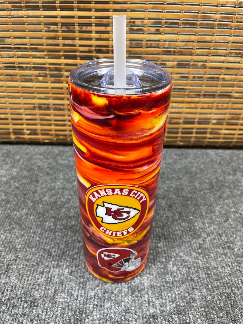 May include: A red and yellow stainless steel tumbler with a Kansas City Chiefs logo. The tumbler has a clear lid and a straw.
