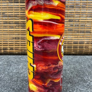 May include: A red, yellow and white stainless steel tumbler with a Chiefs logo and the word "Chiefs" in yellow letters. The tumbler has a swirling, abstract design.