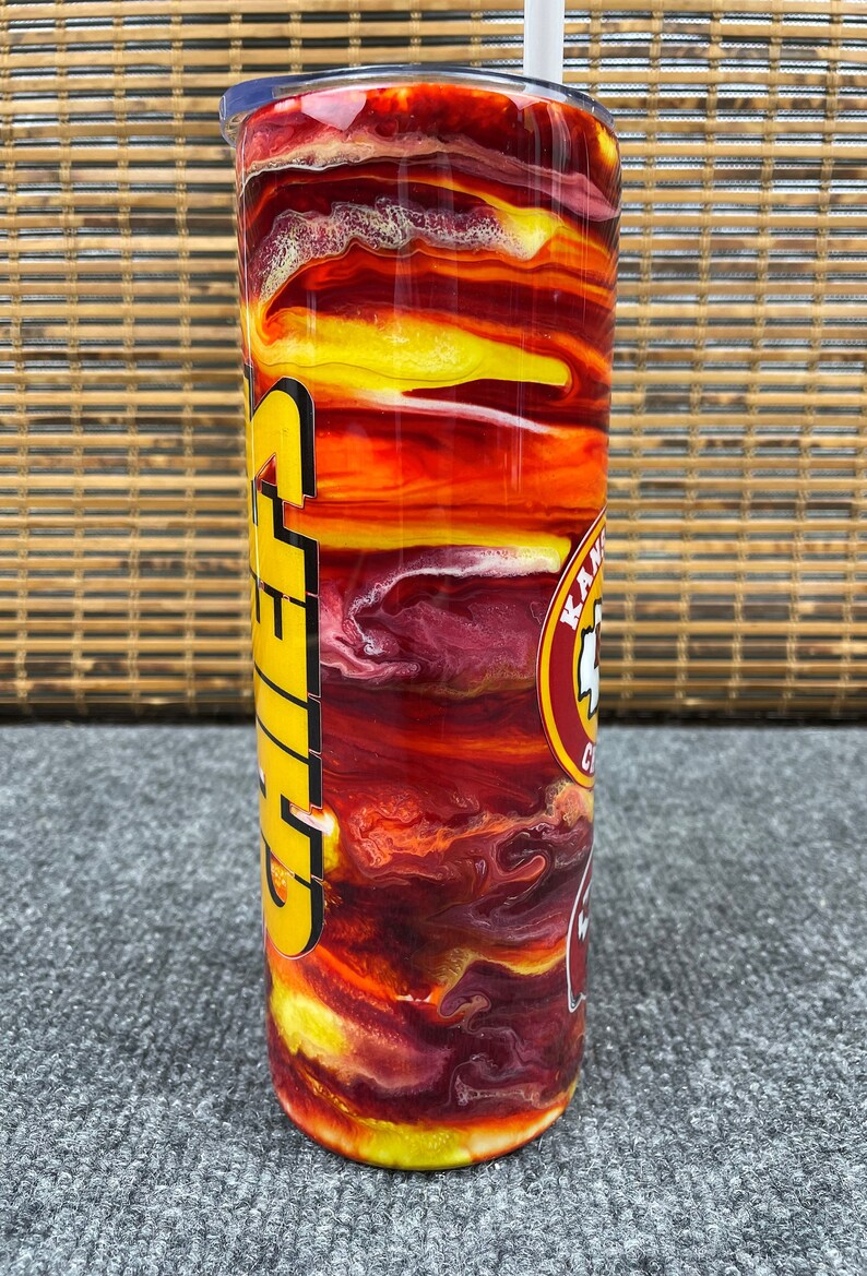 May include: A red, yellow and white stainless steel tumbler with a Chiefs logo and the word "Chiefs" in yellow letters. The tumbler has a swirling, abstract design.