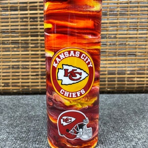 May include: A red and yellow stainless steel tumbler with a Kansas City Chiefs logo and a football helmet. The tumbler has a swirl pattern.