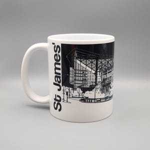 May include: White ceramic mug with a black and white illustration of St. James' Park, a football stadium, on the side. The text "St. James'" is printed vertically on the left side of the mug.