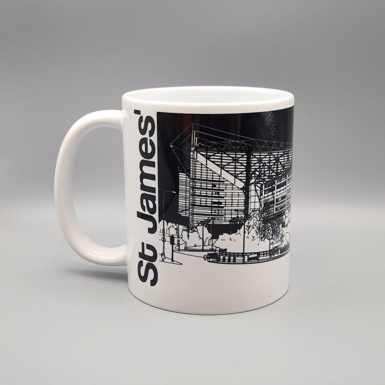 May include: White ceramic mug with a black and white illustration of St. James' Park, a football stadium, on the side. The text "St. James'" is printed vertically on the left side of the mug.