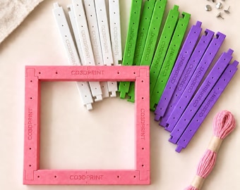 Op de afbeelding: Een vierkante framekit met een roze basis, voorzien van witte, groene en paarse in elkaar grijpende kunststof staven met het label CO3DPRINT. De set bevat kleine metalen pinnen en een bundel roze borduurgaren voor montage en knutselwerk.