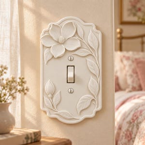 May include: A cream-colored light switch plate featuring a raised, sculpted floral design with a large blooming flower at the top, a closed bud at the bottom left, and leafy vines extending along the right side, secured by two metal screws.