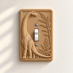 May include: A rectangular light switch plate in a tan, matte finish featuring a raised, embossed relief of a long-necked dinosaur standing next to a tall fern plant. The plate includes a central white toggle switch and two silver screws.