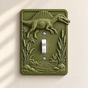 May include: A rectangular olive green light switch plate featuring a raised relief design of a Spinosaurus dinosaur above a swamp scene with cattails, rocks, and water. A white toggle switch is centered between two silver metal screws.