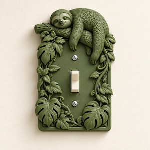 May include: A rectangular olive green light switch cover featuring a sculpted sloth resting on a tree branch. The border is decorated with raised monstera leaves and vines. A single cream-colored toggle switch is centered with two silver screws.