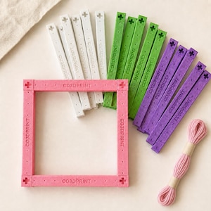 May include: A square frame assembled from pink plastic bars with the text CO3DPRINT, accompanied by loose white, green, and purple bars featuring the same text and cross-shaped ends, plus a bundle of pink embroidery thread for crafting projects.