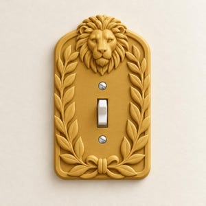 May include: A rectangular gold-colored light switch plate featuring a sculpted lion head at the top and a laurel wreath border that meets at a bow at the bottom. The plate includes a central white toggle switch and two silver-colored screws.