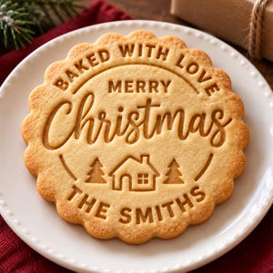 May include: A round, scalloped-edge sugar cookie with an embossed design featuring the text "BAKED WITH LOVE," "MERRY CHRISTMAS," and "THE SMITHS," along with a central graphic of a small house flanked by two pine trees.