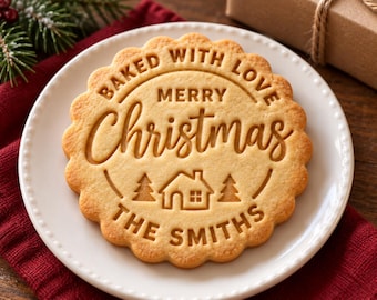 May include: A round, scalloped-edge sugar cookie with an embossed design featuring the text "BAKED WITH LOVE," "MERRY CHRISTMAS," and "THE SMITHS," along with a central graphic of a small house flanked by two pine trees.