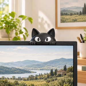 May include: A black cat-shaped monitor topper featuring large white eyes and two small paws resting on the top edge of a computer screen. The cat has a smooth, matte finish and pointed ears, designed to sit securely on the frame of a display.