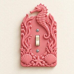 May include: A rectangular light switch cover in a matte coral pink finish featuring a raised, sculpted seahorse at the top, surrounded by intricate seaweed, coral, and seashell motifs along the edges. The center includes a cream-colored toggle switch.