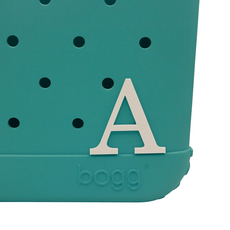 May include: Teal blue tote bag with a white letter "A" on the front. The bag has a textured surface with small holes. The word "bogg" is printed on the bottom of the bag.
