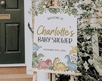 May include: A rectangular sign on a wooden easel featuring the text WELCOME TO Charlotte's BABY SHOWER NOVEMBER 10TH, 20XX. The design includes watercolor illustrations of various dinosaurs in shades of pink, yellow, blue, and green with foliage.