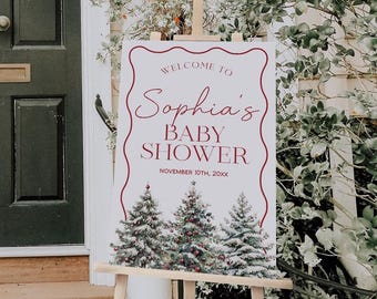 May include: A rectangular white welcome sign for a baby shower featuring a red wavy border, the text "WELCOME TO Sophia's BABY SHOWER NOVEMBER 10TH, 20XX", and a graphic of three snow-covered Christmas trees with red ornaments on a wooden easel.