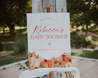 May include: A rectangular white welcome sign for a baby shower featuring the text "WELCOME TO Rebecca's BABY SHOWER" in red and brown lettering, with a date and location below, decorated with a watercolor illustration of orange pumpkins and flowers.