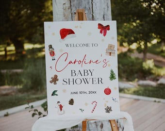 May include: A white rectangular sign on a wooden easel featuring the text "WELCOME TO Caroline's BABY SHOWER JUNE 10TH, 20XX" surrounded by watercolor illustrations of a Santa hat, red bow, nutcracker, gifts, gingerbread man, tree, snowman, and candy cane.