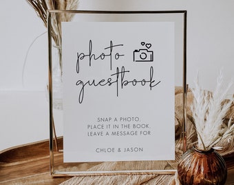 May include: A white sign in a gold frame with the text "photo guestbook" and a camera icon. The sign also includes instructions for guests to snap a photo, place it in the book, and leave a message for Chloe & Jason.