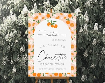 May include: A rectangular baby shower welcome sign featuring an arched white center panel with the text A LITTLE CUTIE IS ON THE WAY WELCOME TO Charlotte's BABY SHOWER JUNE 10TH, 20XX DALLAS, TX surrounded by a peach background with orange fruit patterns.