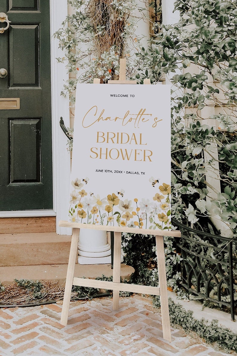 K&ouml;nnte beinhalten: Ein wei&szlig;es Schild mit goldenen Buchstaben auf einem Staffelei, das eine Brautparty f&uuml;r Charlotte ank&uuml;ndigt. Das Schild hat ein Blumenmuster mit Bienen und den Text "Willkommen zur Brautparty von Charlotte am 10. Juni 20XX - Dallas, TX".